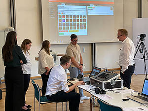 Eine Gruppe von Personen um einen Tisch mit einer großen Projektionsfläche