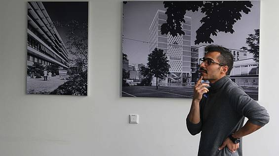 Ein Architekt denkt nach und steht vor Schwarz-Weiß-Bildern, auf denen Gebäude abgebildet sind